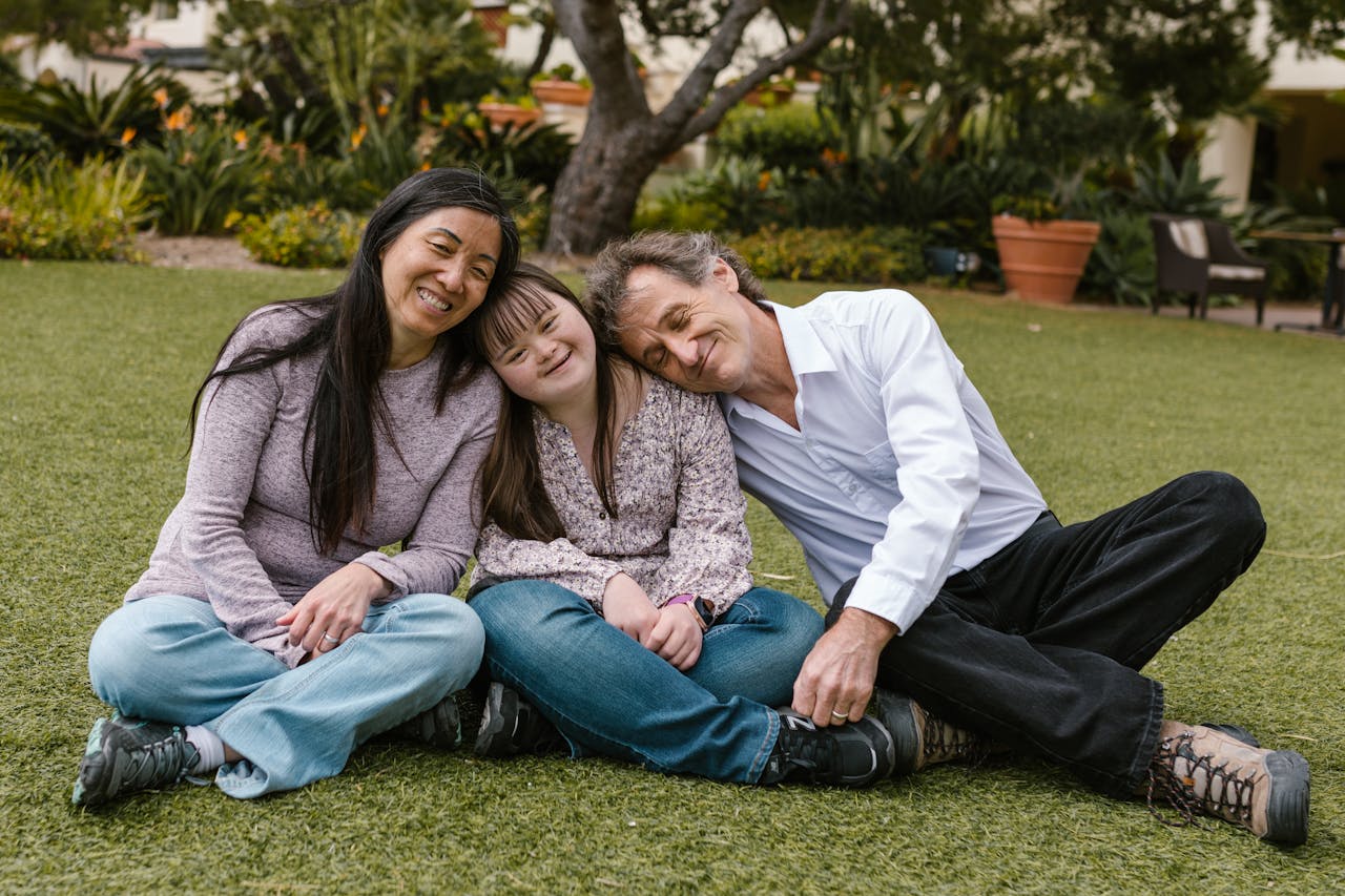 A joyful family sitting on the grass, embracing and smiling together outdoors.